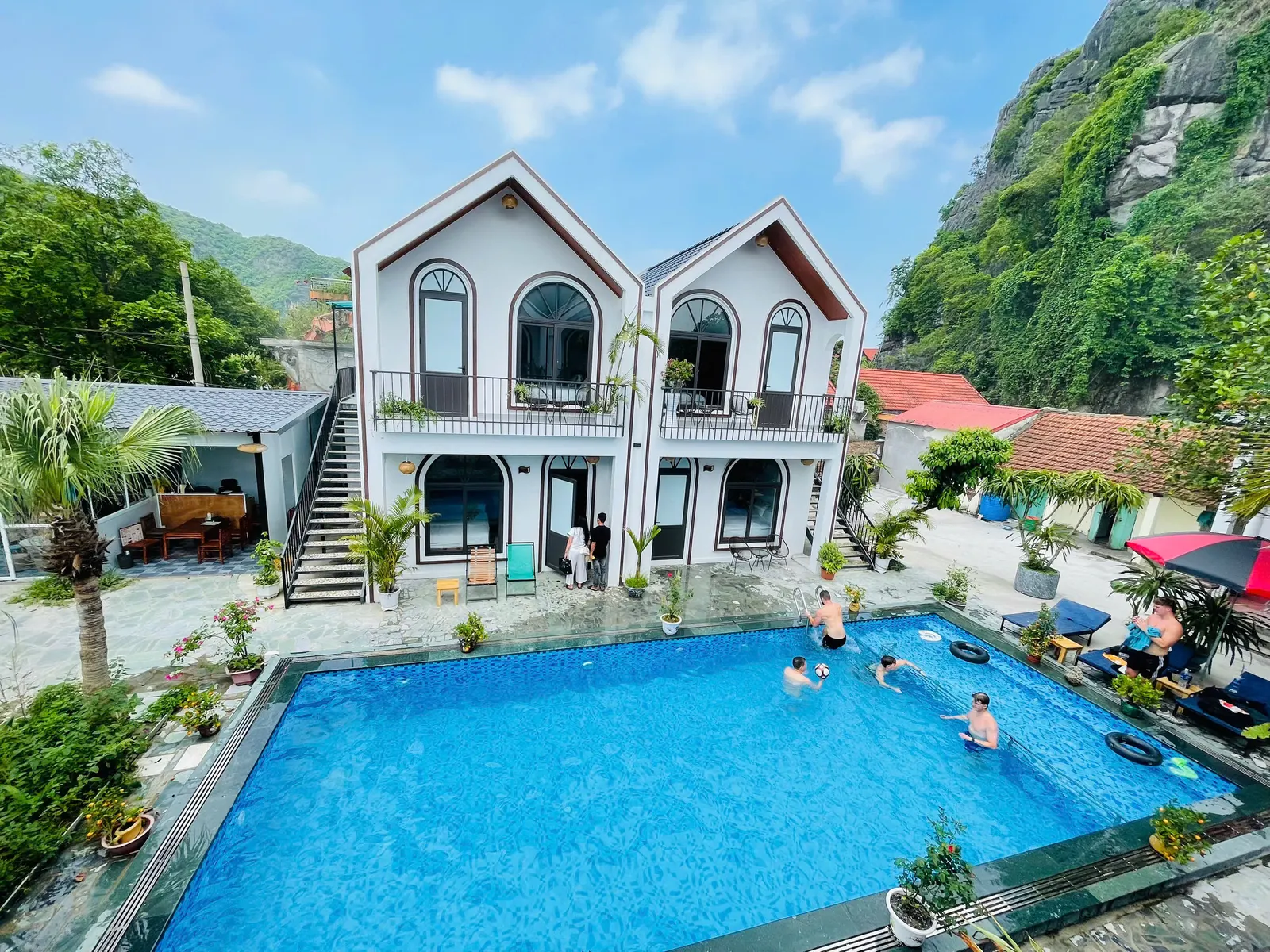 Outdoor pool and white homestay buildings beneath limestone mountains